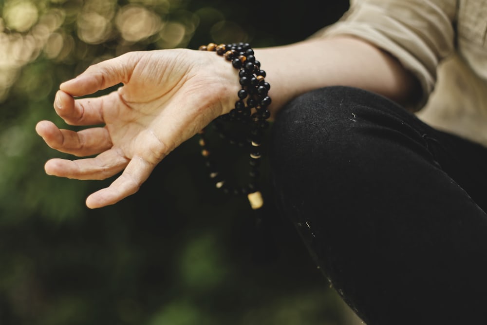Geöffnete, entspannte Hand einer meditierenden Person mit Holzperlenarmband vor grünem Hintergrund