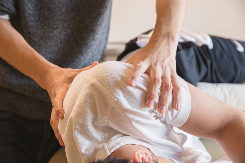 Therapeutin behandelt mit beiden Händen Schulter und oberen Rücken eines liegenden Patienten
