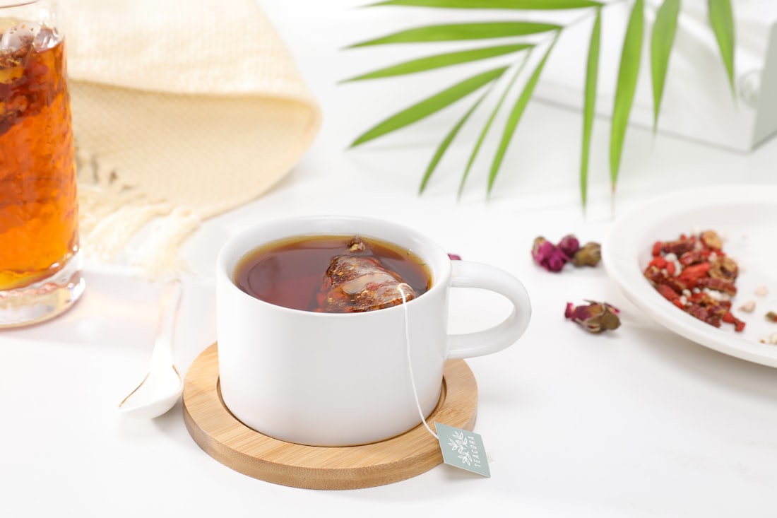 Tasse frisch aufgebrühter Kräutertee neben getrockneten Blüten und Beeren auf hellem Tisch